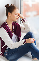 Image showing sad pretty teenage girl sitting on windowsill