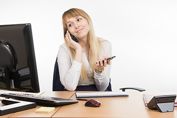 Image showing Happy secretary looked at the computer screen talking on the phone working and holding a cell