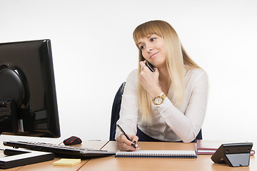 Image showing Upset secretary writing in a notebook the information obtained over the phone and looked at the screen