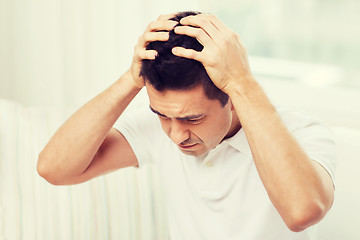 Image showing unhappy man suffering from head ache at home