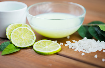 Image showing close up of body lotion in bowl and limes on wood