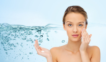 Image showing young woman applying cream to her face