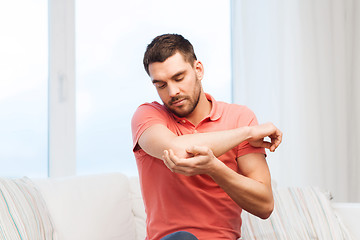 Image showing unhappy man suffering from pain in hand at home