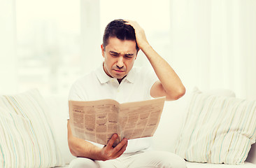 Image showing sad man reading newspaper at home