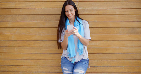 Image showing Woman texting while leaning against wall