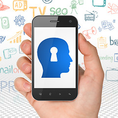 Image showing Advertising concept: Hand Holding Smartphone with Head With Keyhole on display