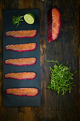 Image showing Sliced salmon fillet, sauteed with beetroot juice over black slate surface.