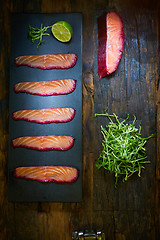 Image showing Sliced salmon fillet, sauteed with beetroot juice over black slate surface.