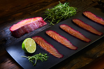 Image showing Sliced salmon fillet, sauteed with beetroot juice over black slate surface.