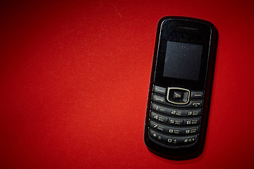 Image showing Old black cell phone on the red background.