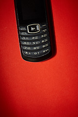 Image showing Old black cell phone on the red background.