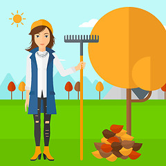 Image showing Woman with rake standing near tree and heap of autumn leaves.