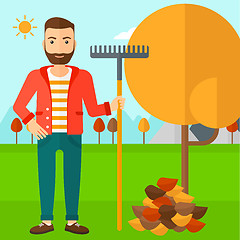 Image showing Man with rake standing near tree and heap of autumn leaves.