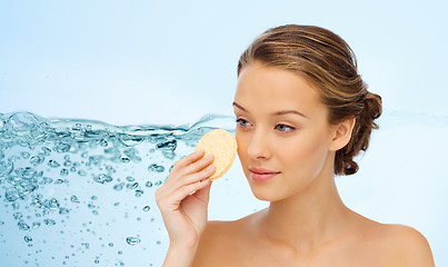 Image showing young woman cleaning face with exfoliating sponge