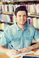 Image showing happy student writing to notebook in library