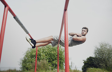 Image showing young man doing sit up on parallel bars outdoors