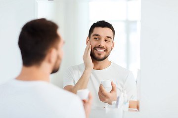 Image showing happy young man applying cream to face at bathroom