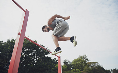 Image showing young man jumping on horizontal bar outdoors