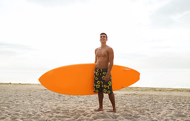 Image showing smiling young man with surfboard on beach