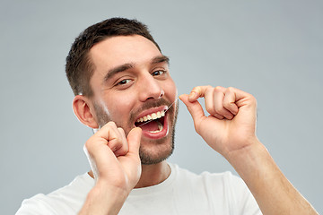 Image showing man with dental floss cleaning teeth over gray