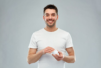 Image showing happy young man with cream jar over gray