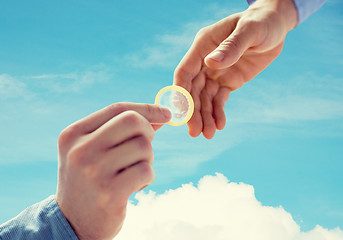 Image showing close up of male gay couple hands giving condom