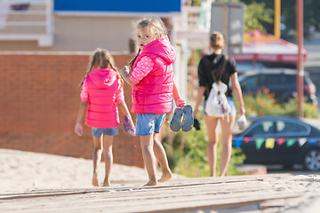 Image showing Mother and two daughters are on the wooden flooring in the sand, one girl turned