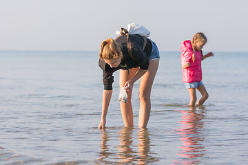 Image showing Woman with child walking along the beach and collect seashells