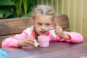 Image showing Six-year girl drinks tea from a spoon breakfast on the veranda