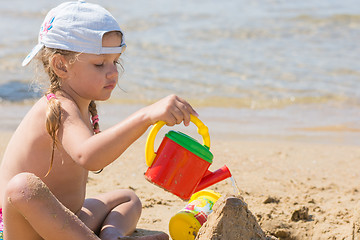 Image showing Four-year girl pouring water on sand castle