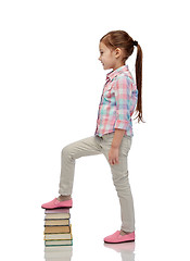 Image showing happy little girl stepping on book pile