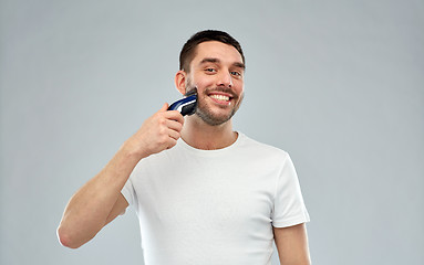 Image showing smiling man shaving beard with trimmer over gray