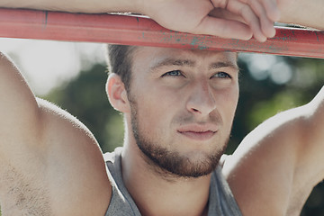 Image showing young man exercising on horizontal bar outdoors