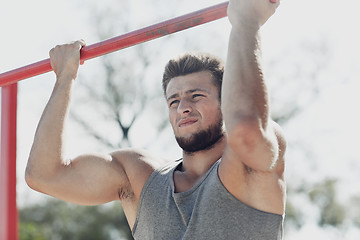 Image showing young man exercising on horizontal bar outdoors