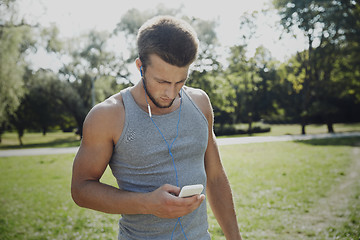 Image showing young man with earphones and smartphone at park