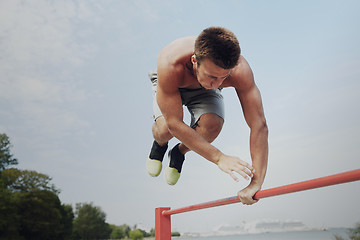 Image showing young man exercising on horizontal bar outdoors