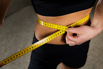 Image showing close up of woman measuring waist by tape in gym