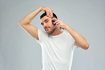 Image showing smiling man shaving beard with trimmer over gray