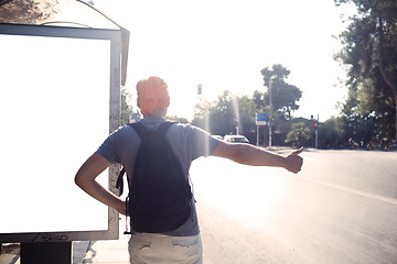 Image showing Man standing near bus stop thumbing a lift