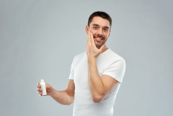 Image showing happy young man applying cream or lotion to face