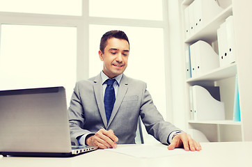 Image showing smiling businessman with laptop and papers