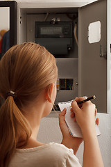 Image showing Young woman rewrites the electrical meter readings