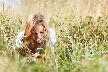 Image showing Girl is writing sms on the phone lying in grass