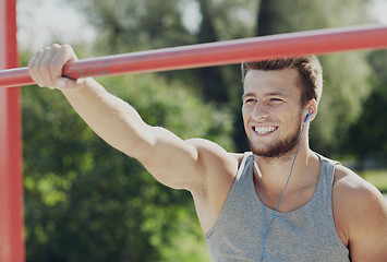 Image showing happy young man with earphones and horizontal bar