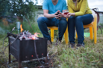 Image showing Couple with tea cups in hands near the smouldering fire