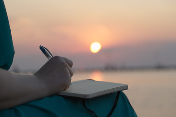 Image showing Woman writing in her diary at sunset