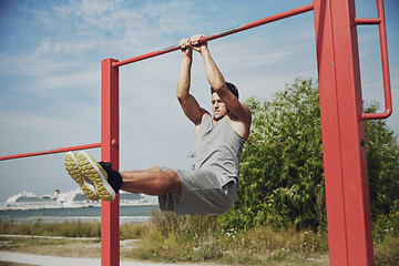 Image showing young man exercising on horizontal bar outdoors