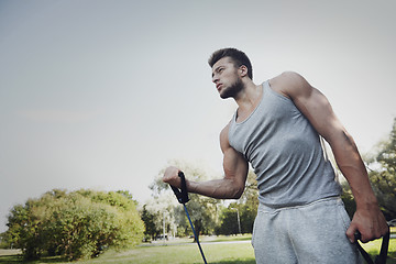 Image showing young man exercising with expander in summer park