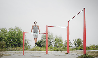 Image showing young man exercising on horizontal bar outdoors