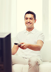 Image showing smiling man with remote control watching tv